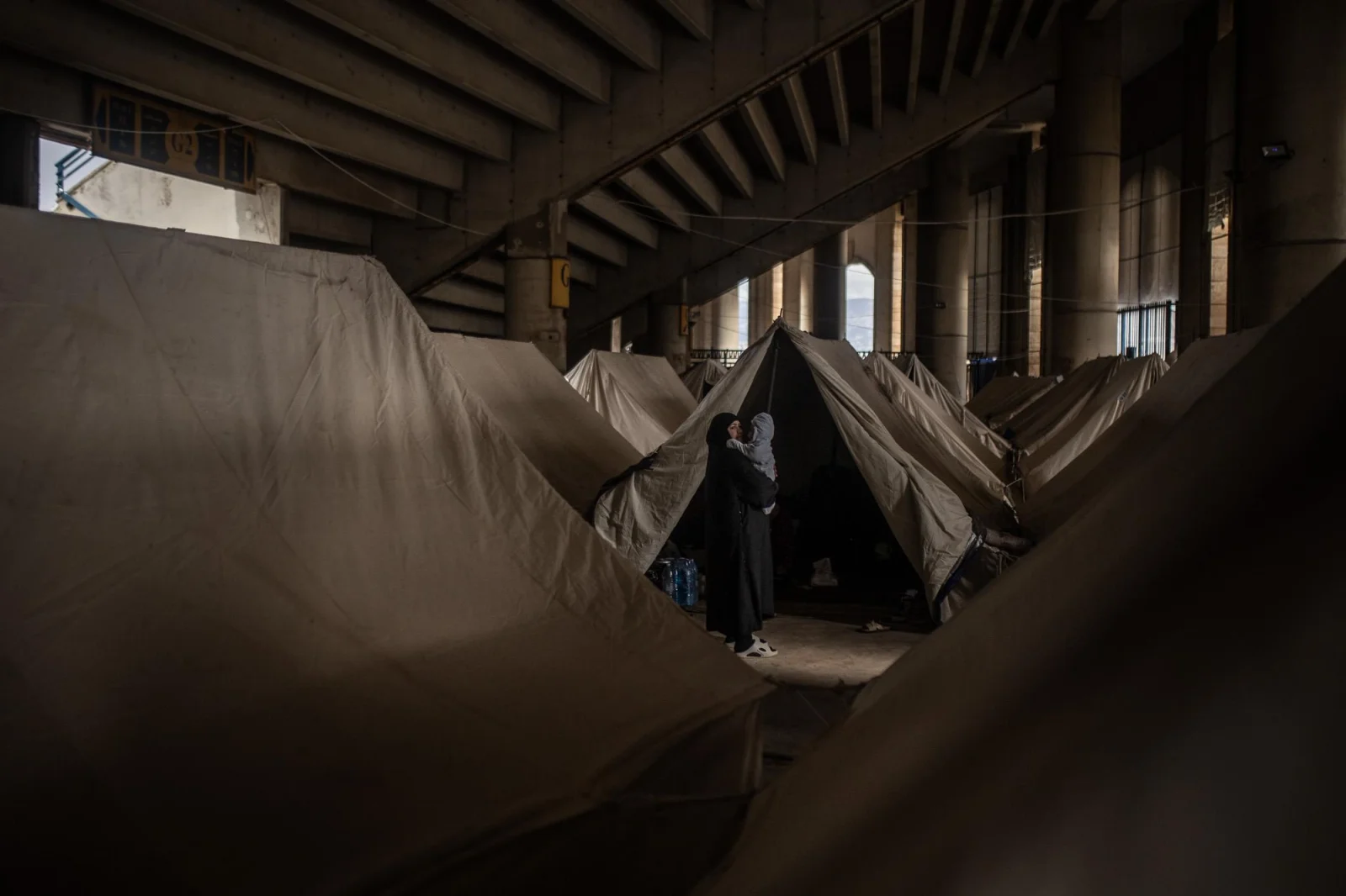 Una mujer sostiene a su bebé frente a su tienda en un campamento improvisado bajo las gradas de un estadio al sur de Beirut. Miles de familias desplazadas por los bombardeos israelíes buscan refugio en instalaciones mientras aguardan el fin de los ataques para regresar a sus hogares. Líbano