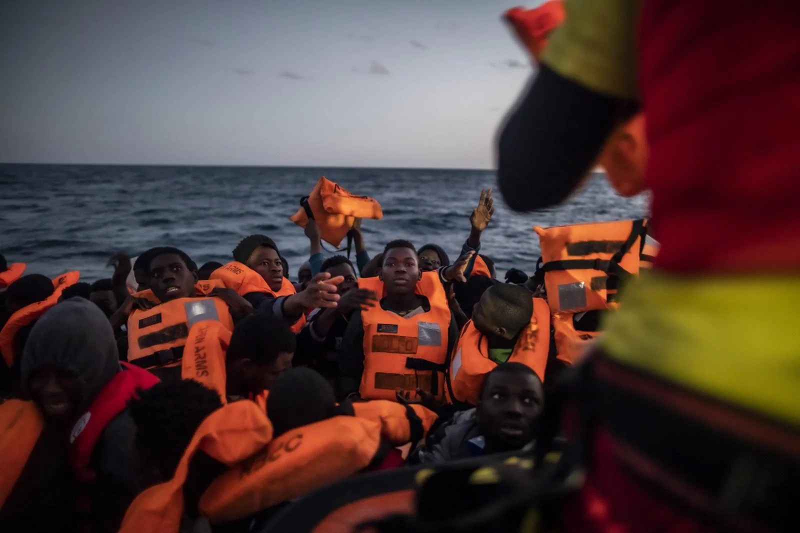 Rescuer Alberto Agrelo distributes the waistcoats to all the migrants, in the centre of the picture, Bamba Bourahima, 14 years old from Ivory Coast Migrants and refugees from different African nationalities wait for assistance aboard an overcrowded rubber boat, as aid workers of the Spanish NGO Open Arms approach them in the Mediterranean Sea, international waters, at 80 miles off the Libyan coast, Saturday Feb. 13, 2021.