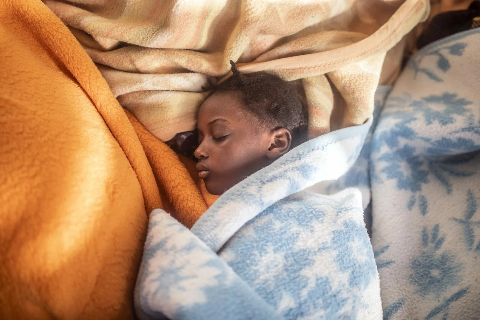 5 year old Timi sleeps between the blankets at her mother's feet, basking in the warmth of the sun's rays after been rescue by the Spanish NGO Open Arms Sunday, Feb. 14, 2021
