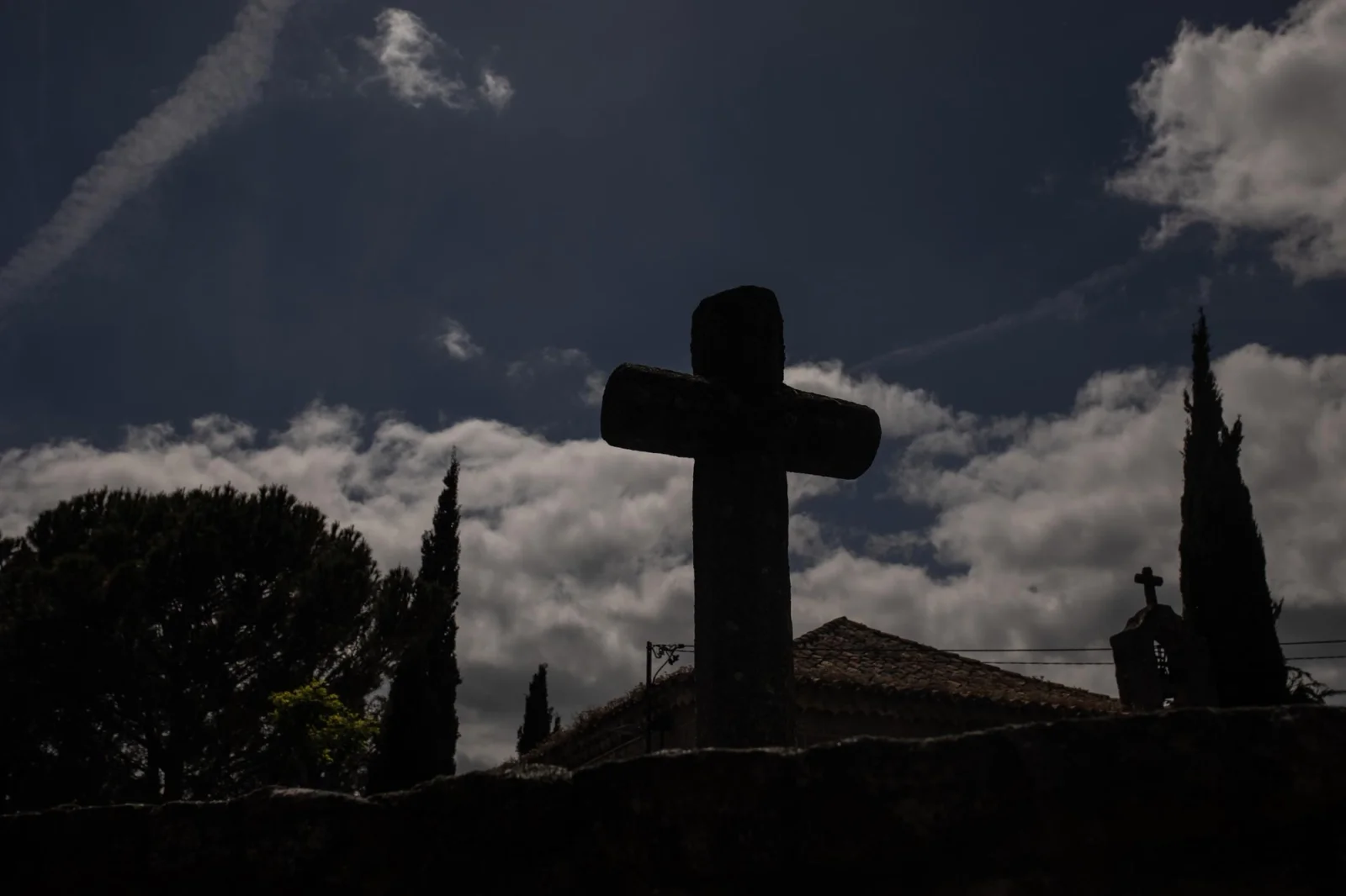 A stone cross stands in silhouette outside the Chapel of
