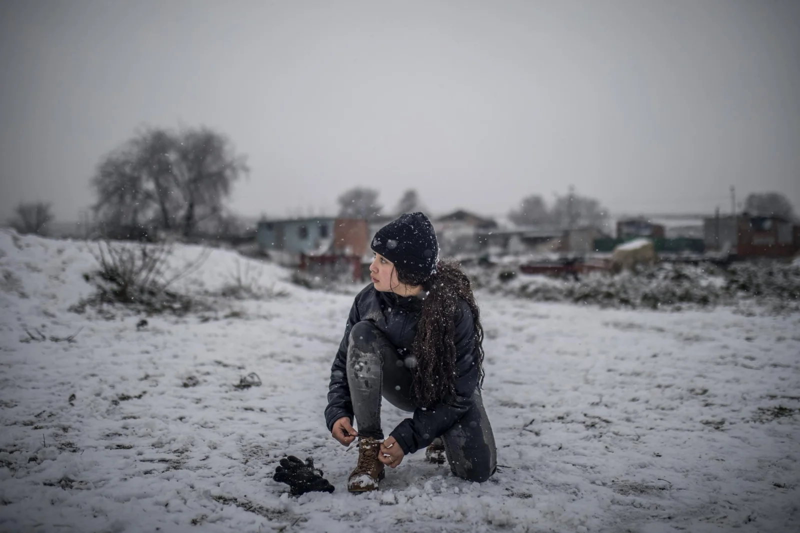 Una niña se ata los cordones mientras juega con sus amigos en la nieve en el Sector VI de la Cañada Real