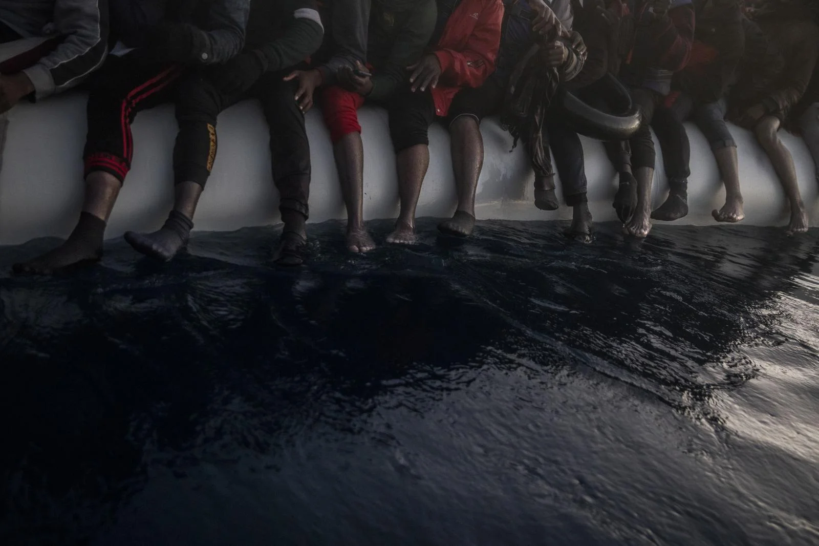Migrants and refugees are seen barefoot in a rubber boat. Migrants and refugees from different African nationalities wait for assistance aboard an overcrowded wooden boat, as aid workers of the Spanish NGO Open Arms approach them in the Mediterranean Sea, international waters, at 80 miles off the Libyan coast, Saturday, Feb. 13, 2021.