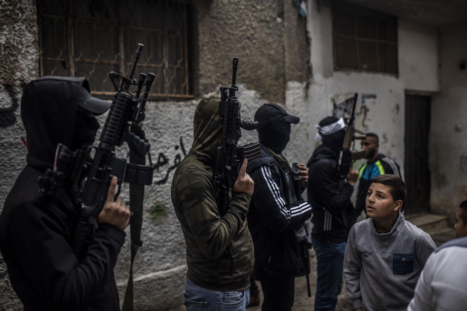 Un joven palestino se cruza con miembros de la resistencia armada en el campo de refugiados de Balata en Nablus
